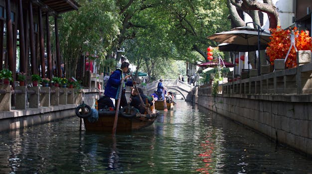 Traditional boat ride along a scenic canal in Suzhou, China under lush trees.