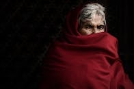 一位裹着红色披肩的老妇人，在黑暗背景下专注地凝视着