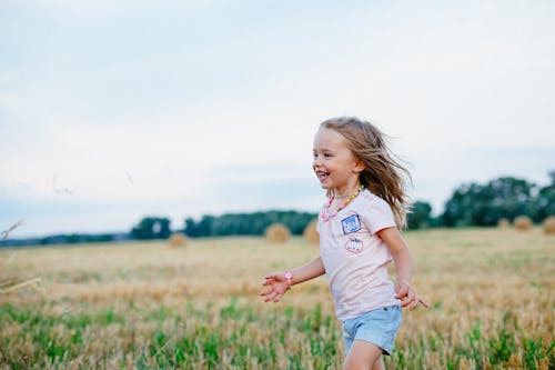 Free Smiling Girl Running Towards Left on Green Field Stock Photo