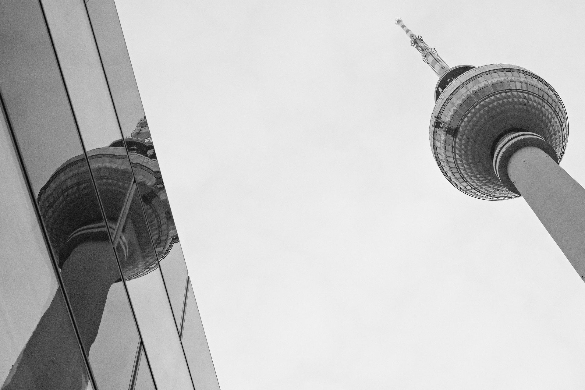 Black and white photo of Berlin TV Tower reflecting in a glass building, urban architectural contrast.