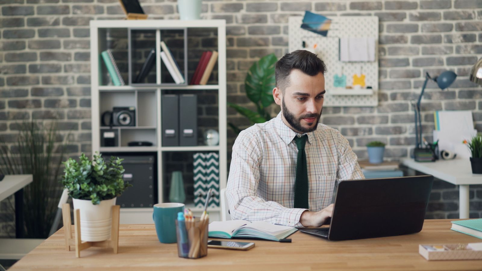 Free Man in a shirt and tie working on his laptop in a modern office setting. Stock Photo