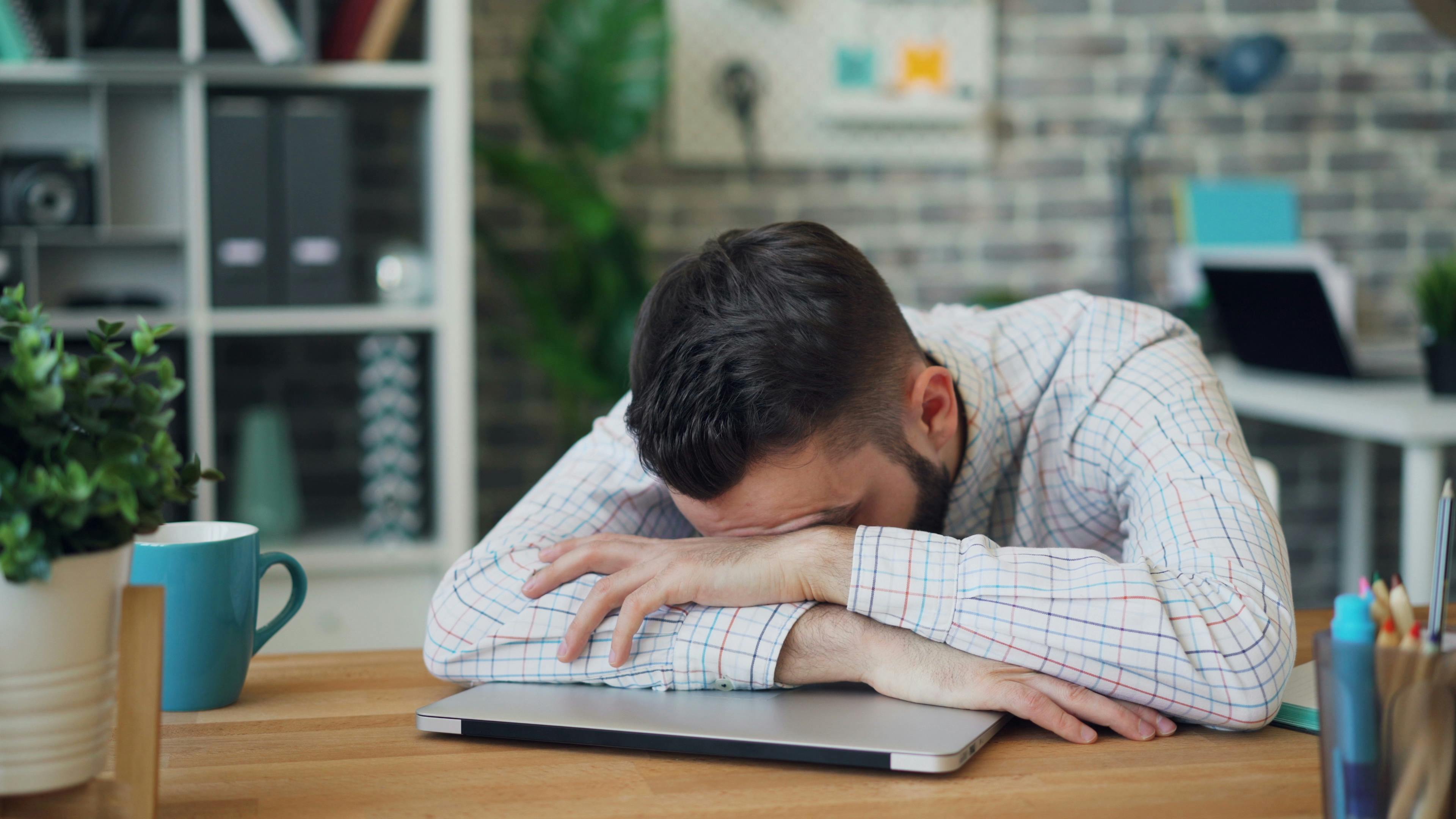 Tired office worker resting head on laptop at desk in a modern office.