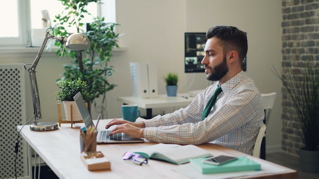 A professional businessman working diligently at his desk with a laptop in a modern office setting.