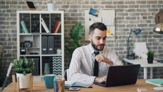 Man engaged in work on laptop in a stylish office setting with books and plants.