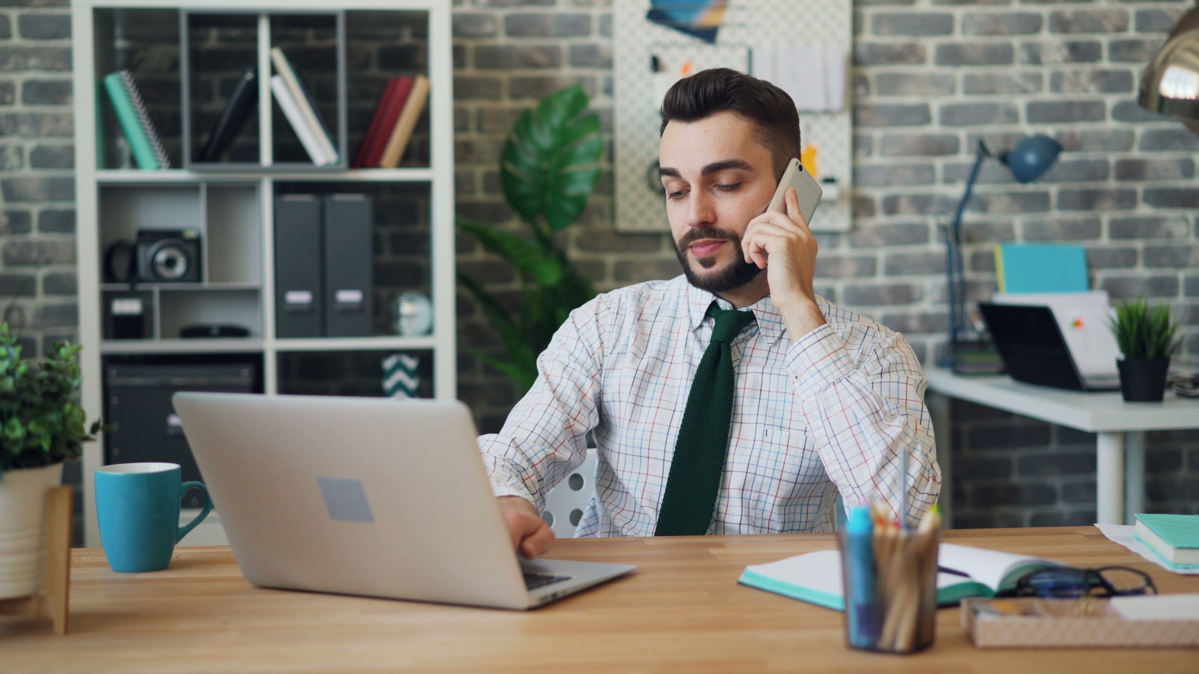 Professional man multitasking with laptop and smartphone in a modern office setup.