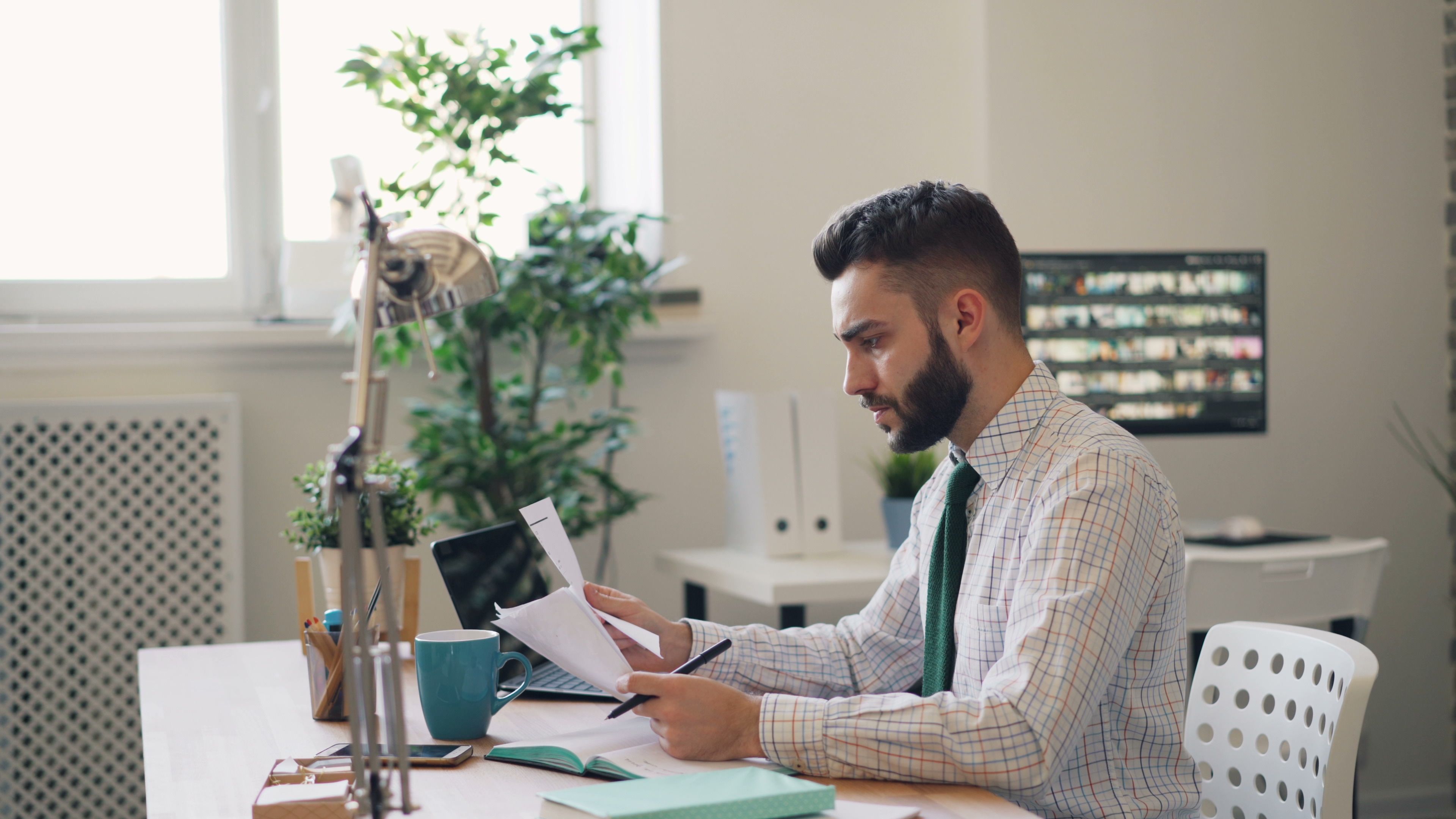 Focused man reviewing documents at a modern office desk with plants.
