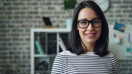 Portrait of a smiling woman with glasses in a stylish modern office setting — photo by Vitaly Gariev on Pexels