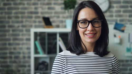 Free Portrait of a smiling woman with glasses in a stylish modern office setting. Stock Photo