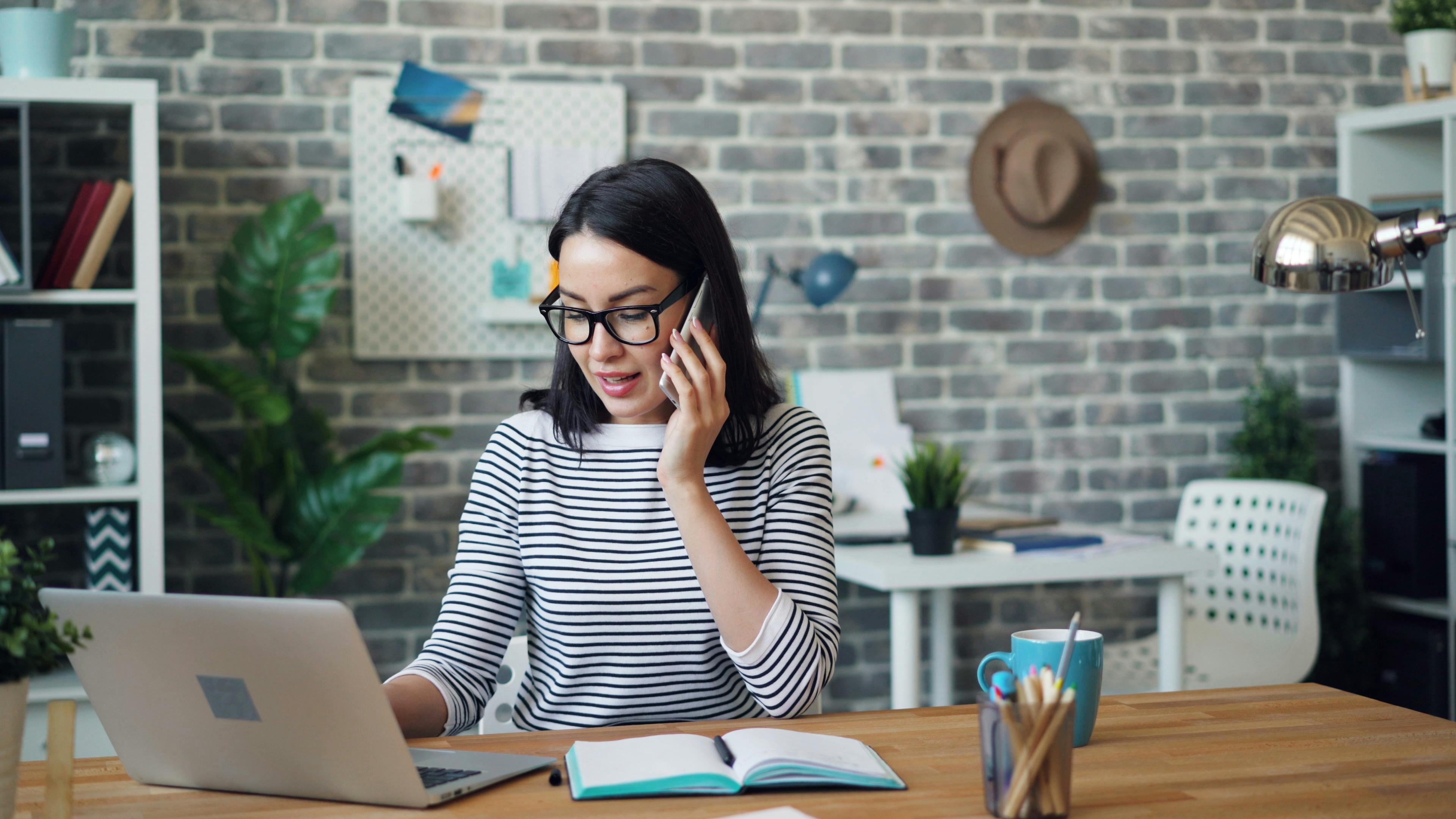 Woman multitasking between laptop and phone in a modern office setting.