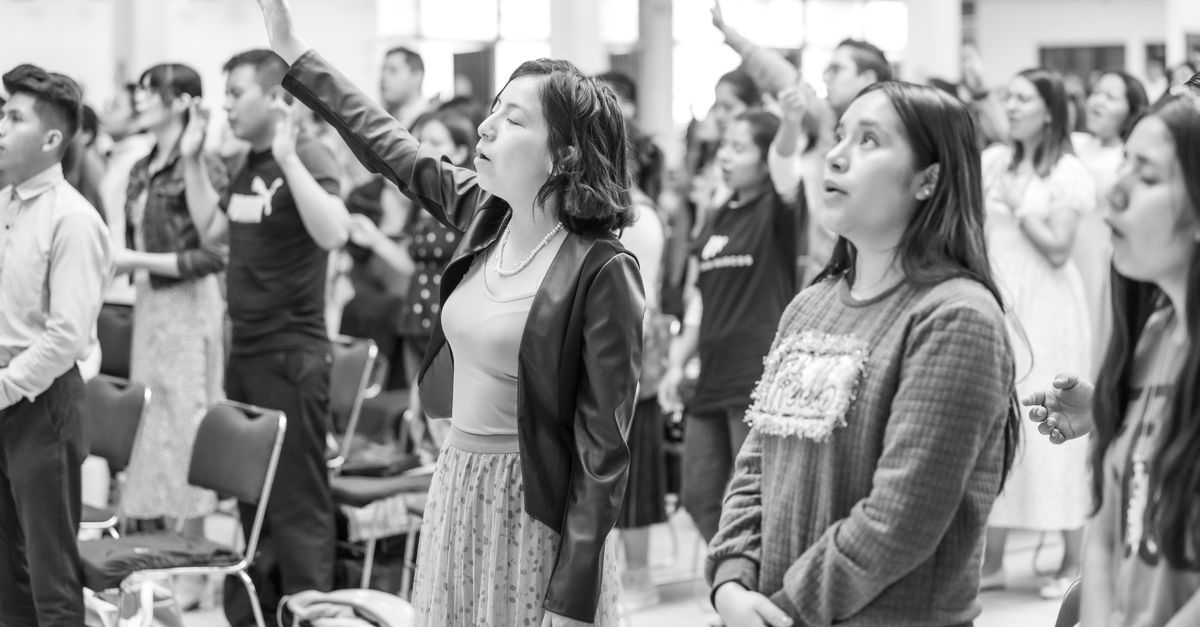 Black and white scene of people gathered for prayer in Ciudad de México, featuring raised arms and standing attendees.