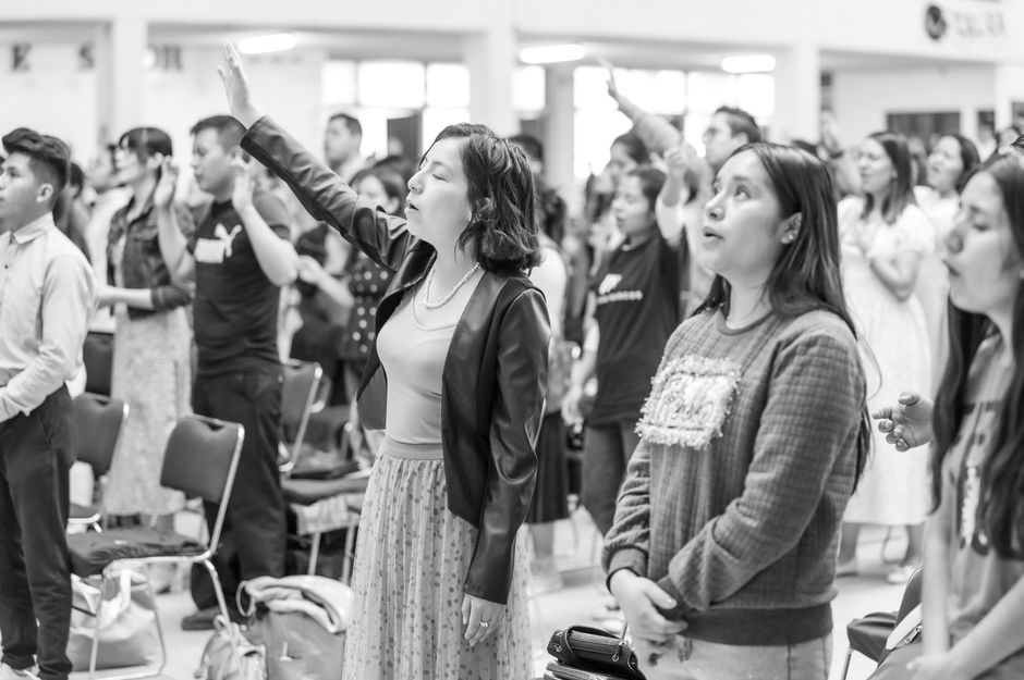 Black and white scene of people gathered for prayer in Ciudad de México, featuring raised arms and standing attendees.