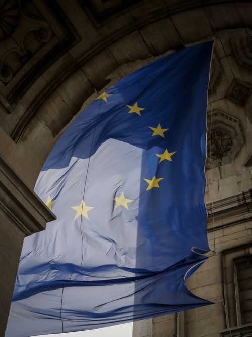 Free European Union flag waving elegantly within a historic stone archway in Brussels. Stock Photo