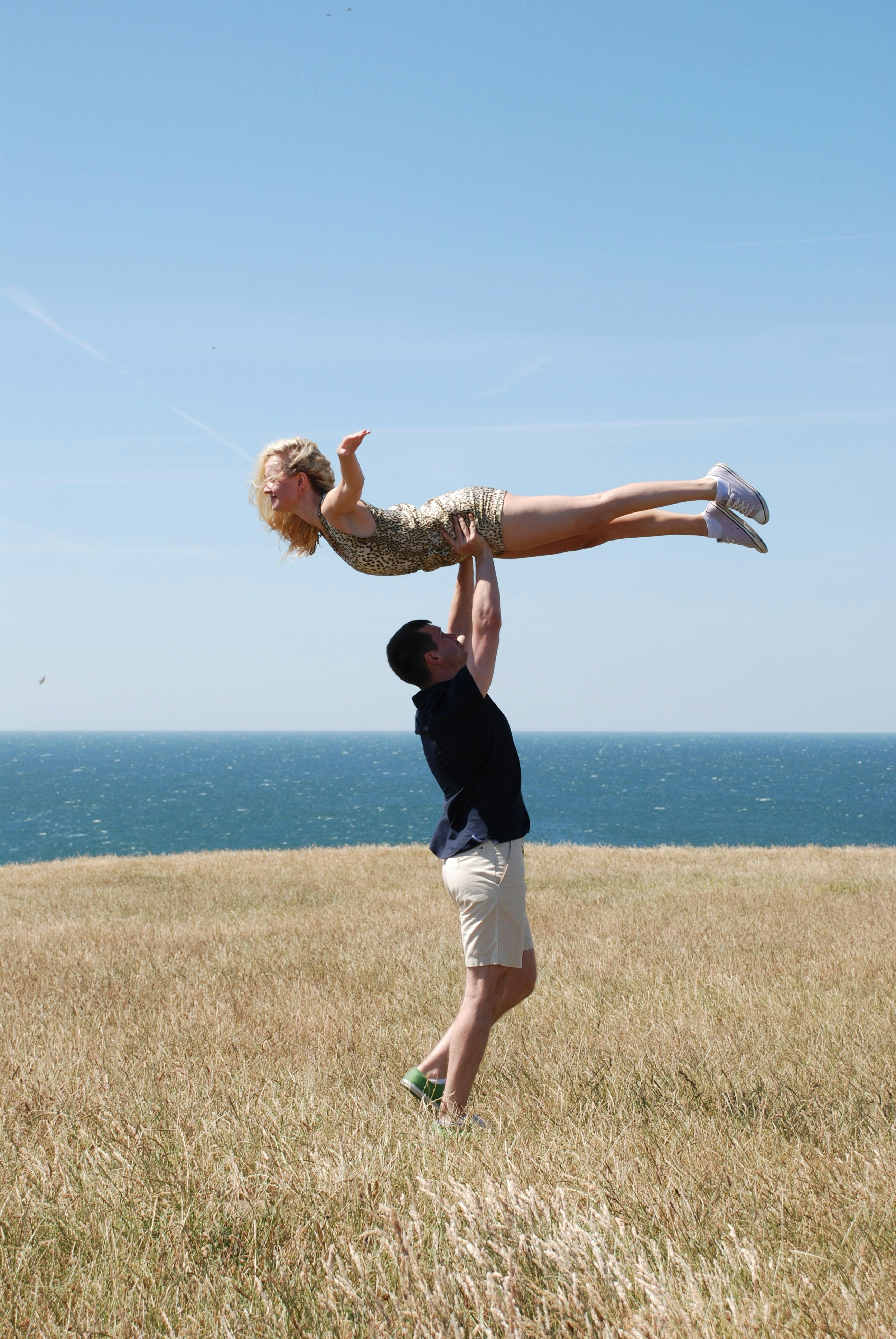 Man Lifting Woman in Open Field Near Body of Water