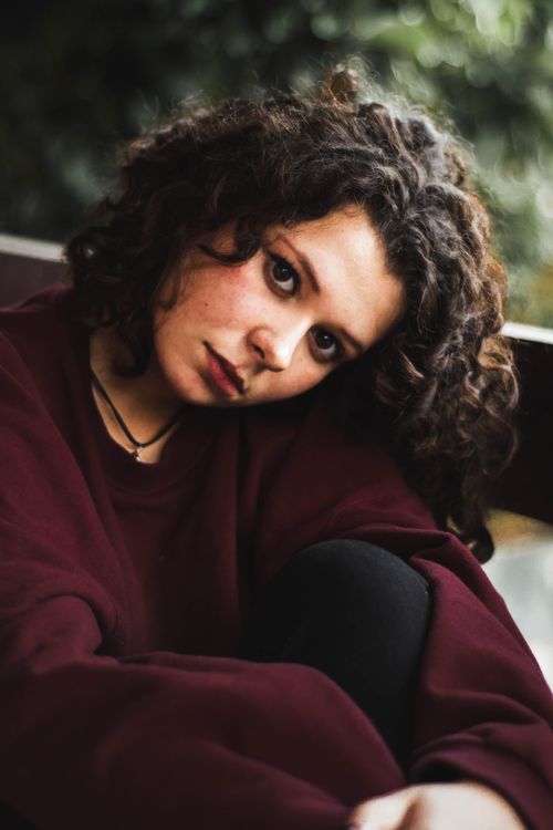 Free Portrait of a woman with curly hair sitting outdoors in a thoughtful pose. Stock Photo