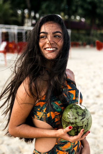 A cheerful woman at the beach holding a coconut, exuding happiness and summer vibes.