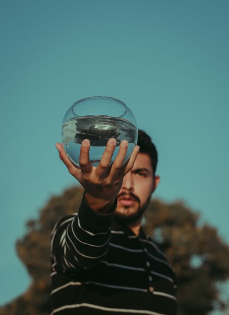 A man holding a fishbowl with clear water, creating a unique visual with a blurred background.