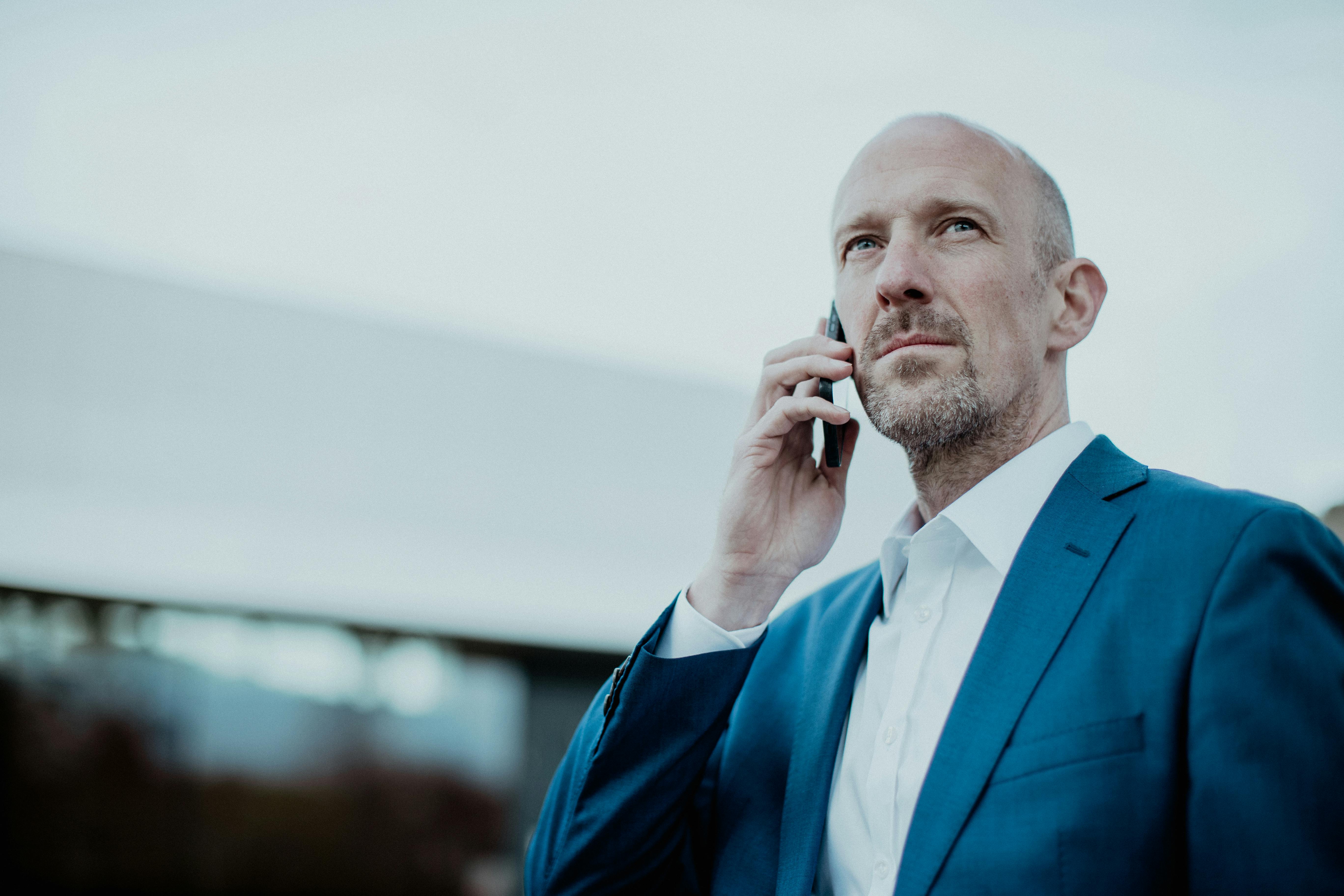 Confident businessman in blue suit talking on smartphone outdoors.