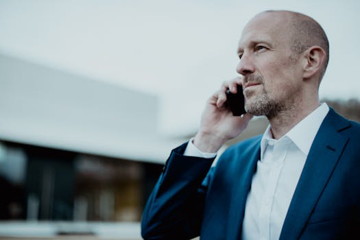 Bald businessman in a blue suit making a call outside, showing professional confidence.