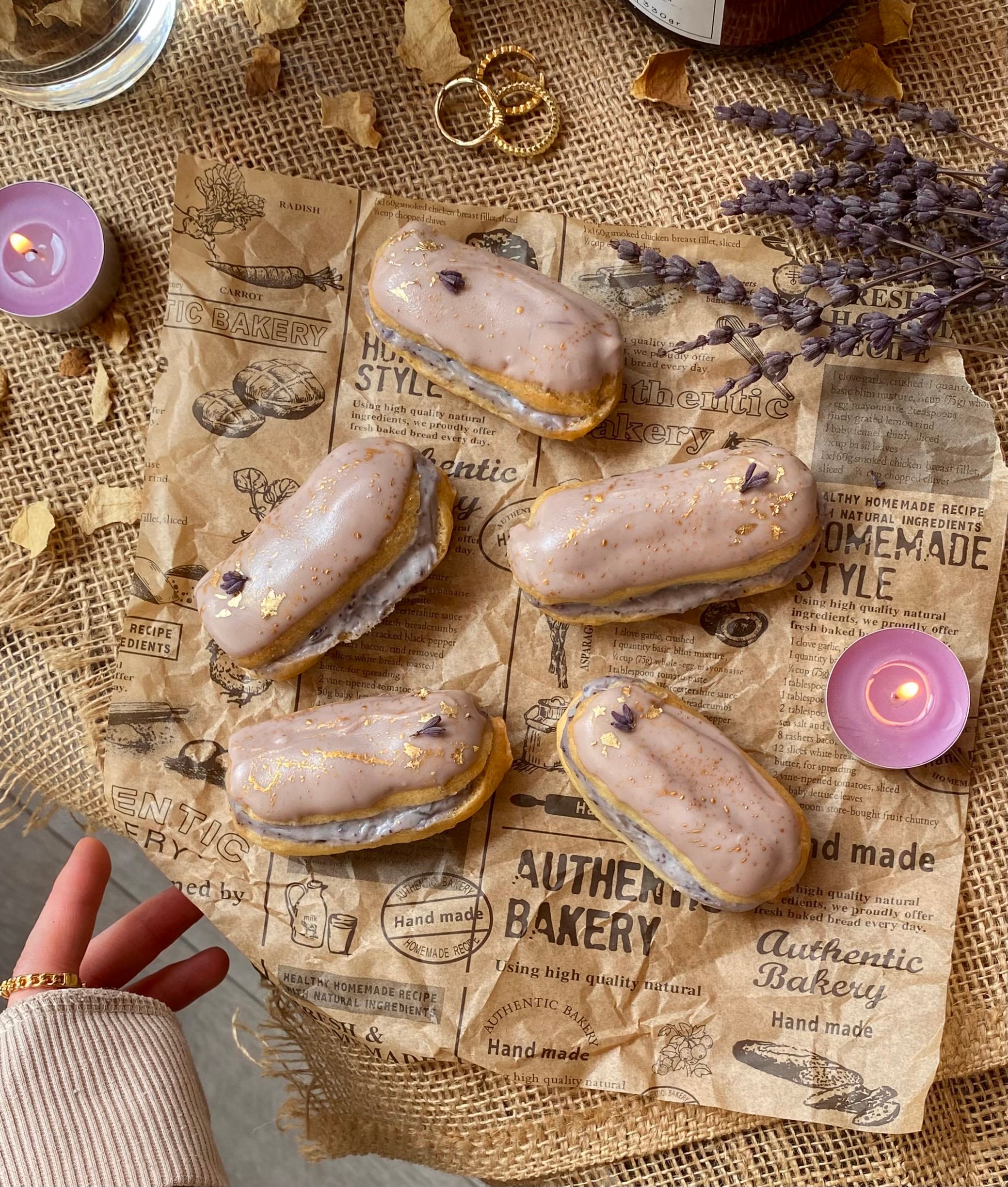 Elegant lavender eclairs on vintage paper with candles and rustic decor.