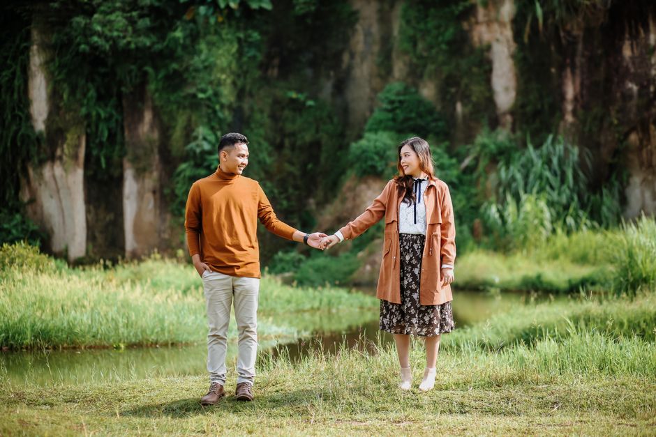 Couple holding hands in a serene outdoor setting, surrounded by lush greenery.