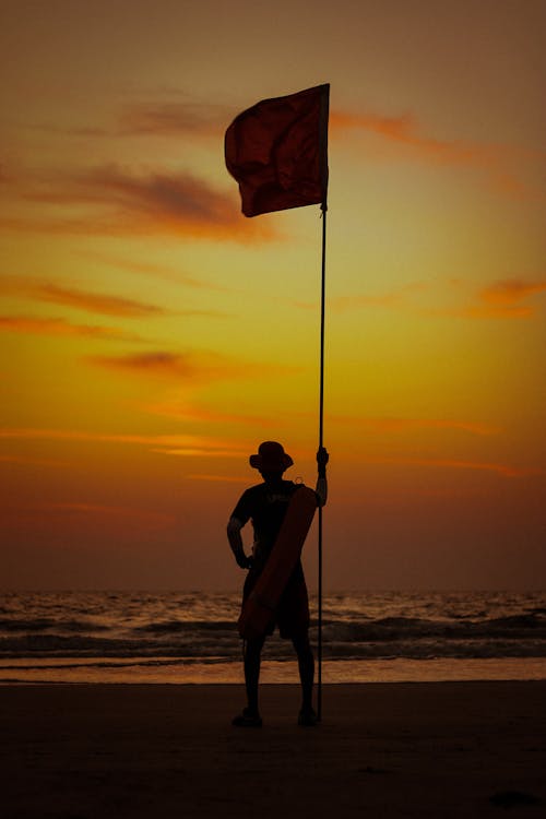 A man standing on a beach holding a red flag