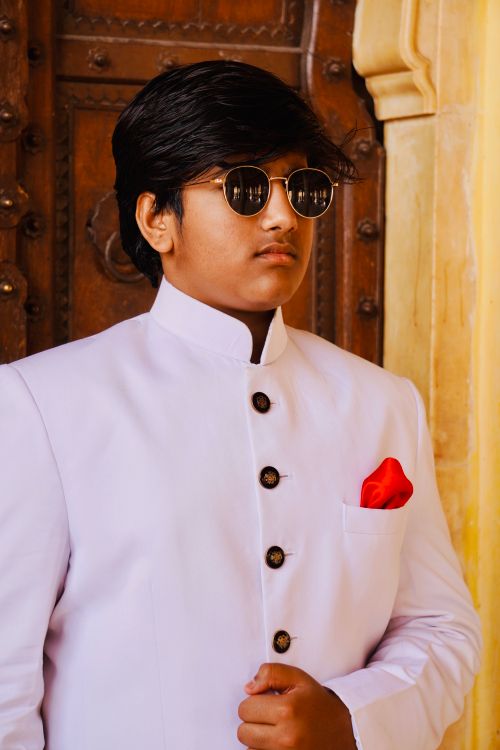 Free A stylish young man in a white suit and sunglasses stands confidently by an ornate door. Stock Photo