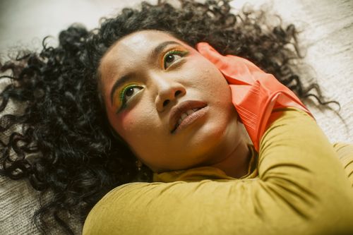 Free Artistic close-up portrait of a woman with curly hair and vibrant makeup, lying on the floor. Stock Photo