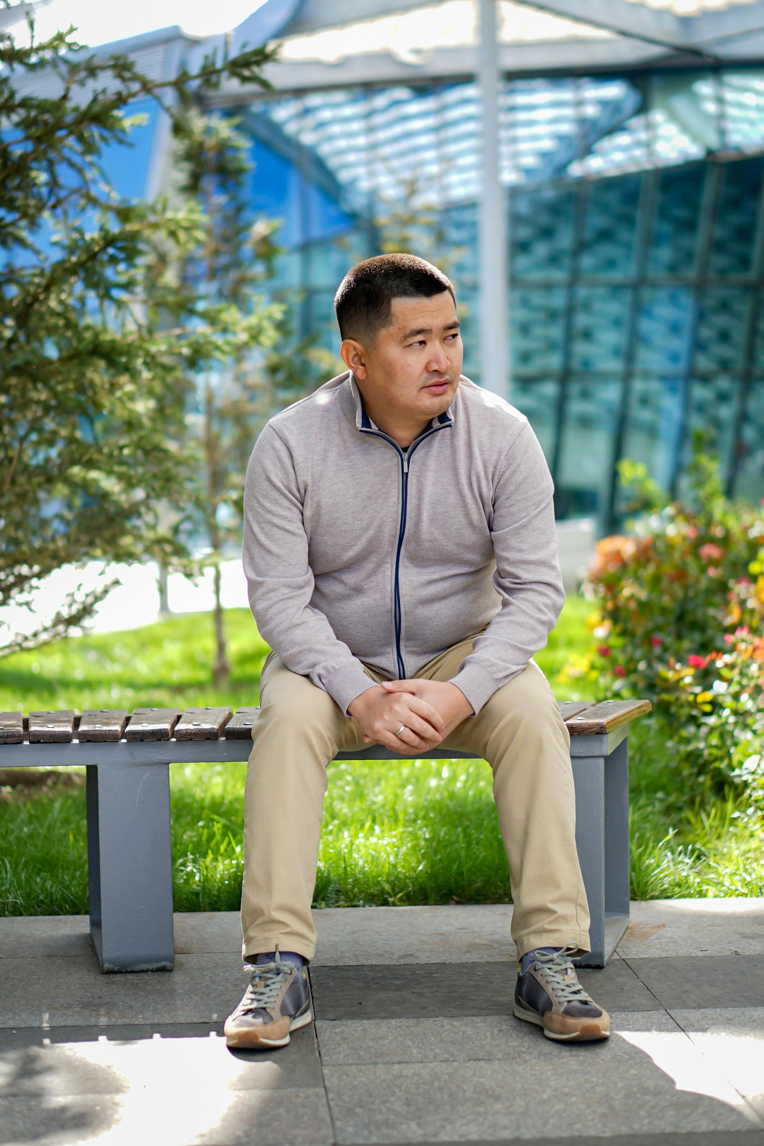 Asian man sitting on a bench near glass building in Astana.