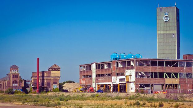 An old industrial factory building with a tower under a clear blue sky, showcasing urban decay.