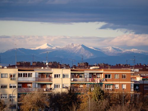 Free Urban view of Madrid with distant snow-capped mountains under a dramatic sky. Stock Photo