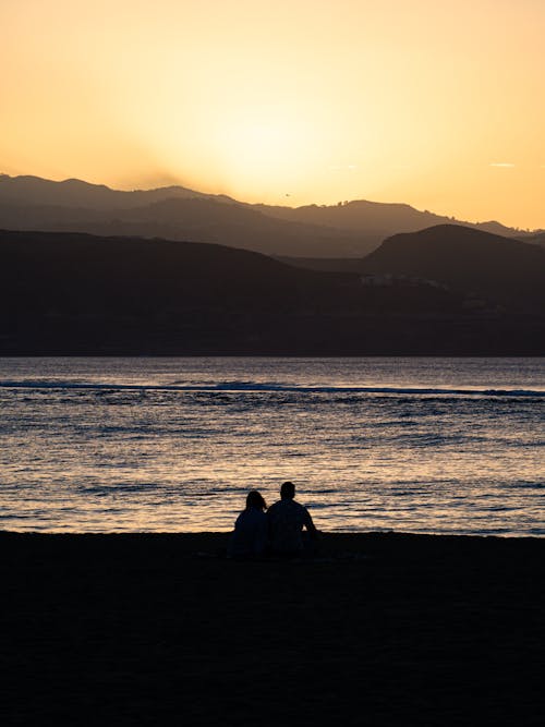 Two people sitting on the beach at sunset