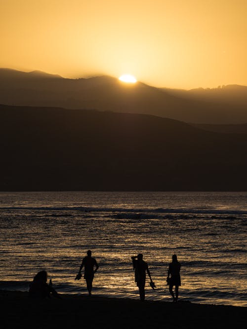 A group of people walking on the beach at sunset