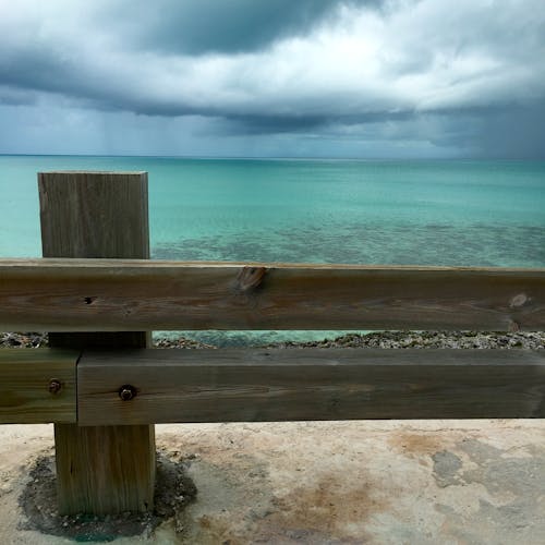 Recinzione In Legno Marrone Vicino Acqua Blu Dell'oceano Sotto Il Cielo Nuvoloso Bianco Durante Il Giorno