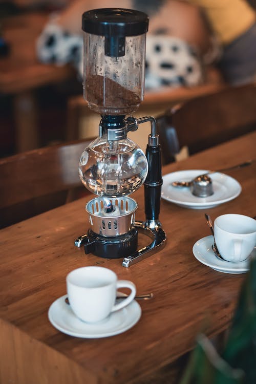A coffee grinder sits on a wooden table with two cups