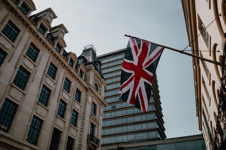 Low angle view of a Union Jack flag with historic and modern buildings in London, UK.