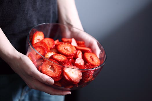 A person holds a glass bowl filled with fresh, sliced strawberries, showcasing healthy and organic food.