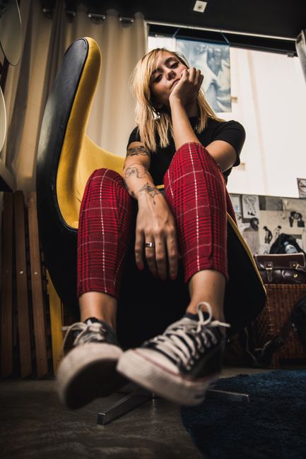 Fashionable woman sitting on a chair, wearing red plaid pants and casual sneakers indoors.