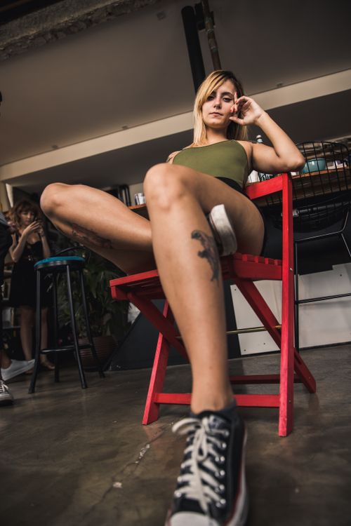 Free Low-angle, artistic portrait of a tattooed woman sitting indoors on a red chair. Stock Photo