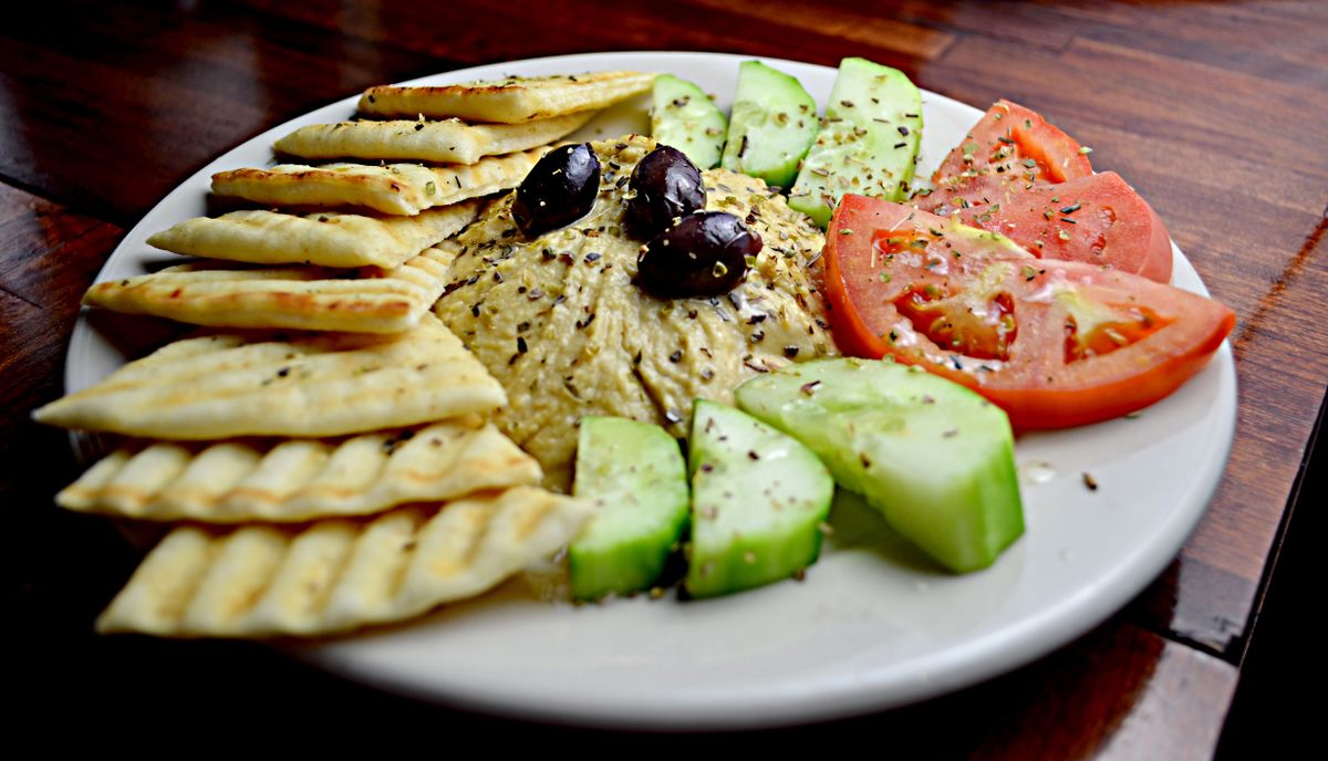 Hummus topped with black olives and herbs, zaatar flatbread strips, cucumber chunks and tomato wedges
