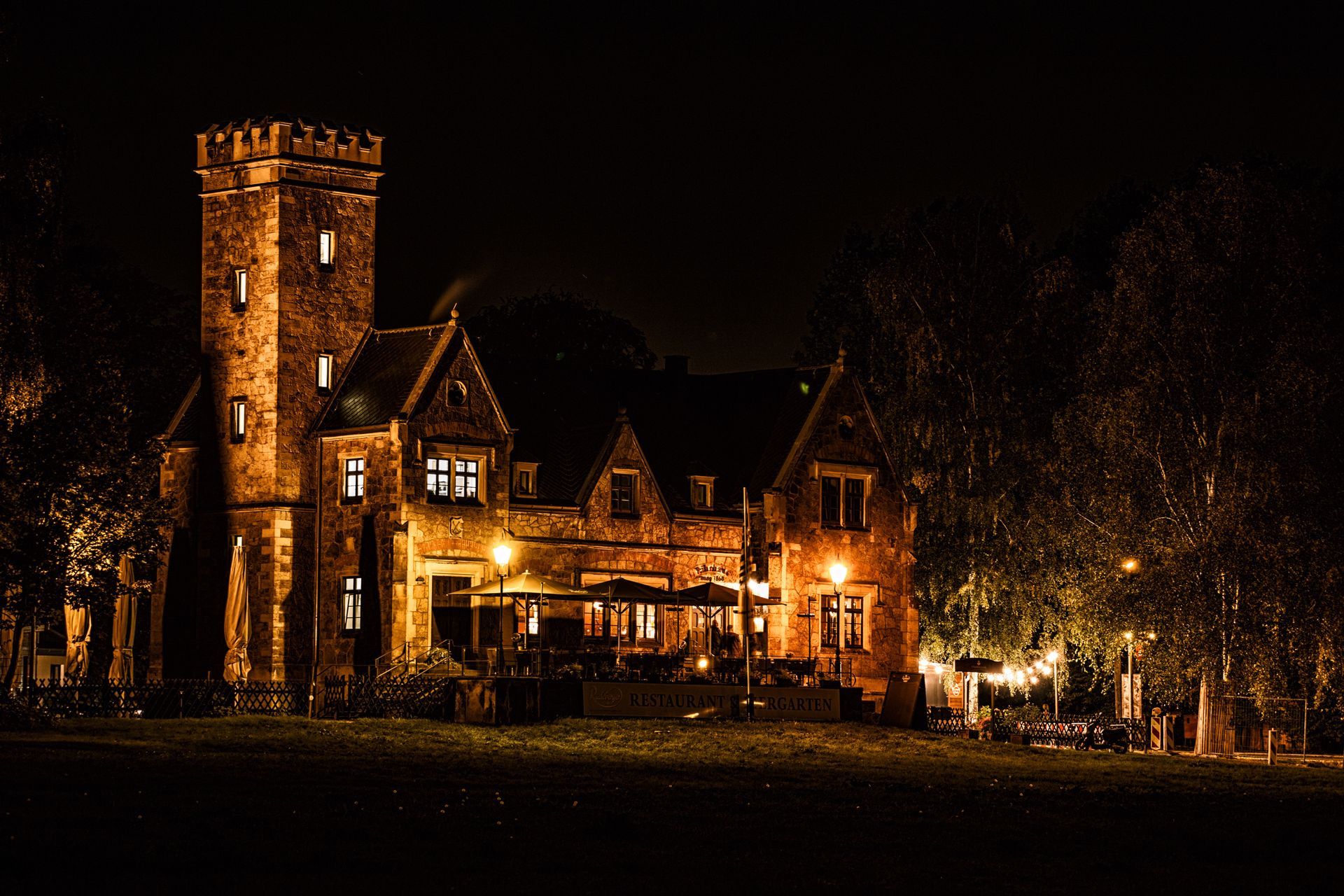 A beautifully lit historic mansion with tower and patio, captured at night, exuding charm and elegance.