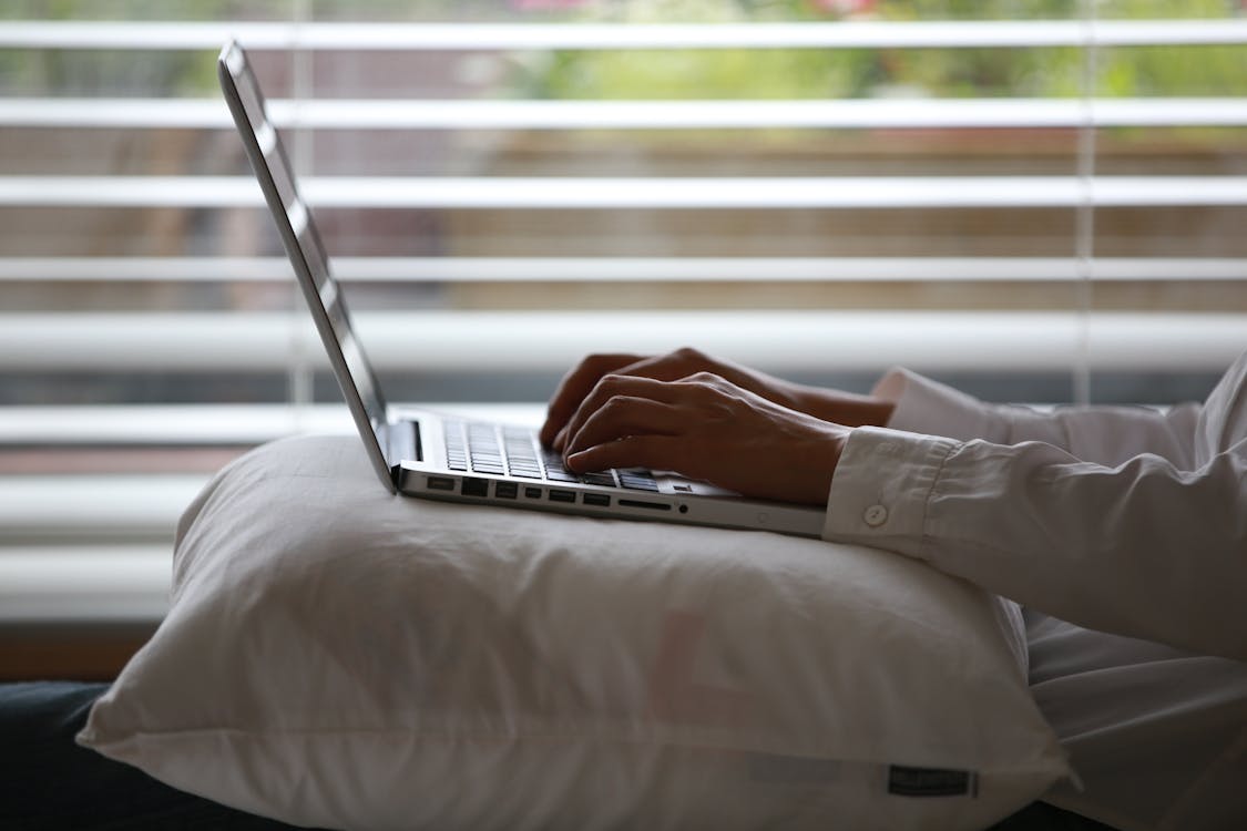 Persona Che Indossa La Camicia Di Vestito Bianco Utilizzando Laptop D'argento Sulla Parte Superiore Del Cuscino Bianco