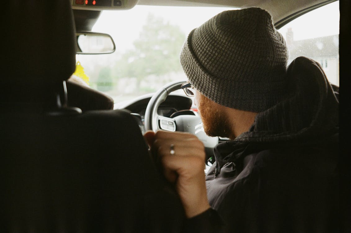 A man in a beanie sits in the back seat of a car