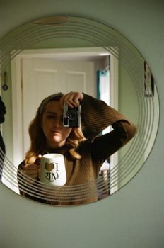 Portrait of a woman holding a 'I Love Cats' mug, taking a mirror selfie indoors.