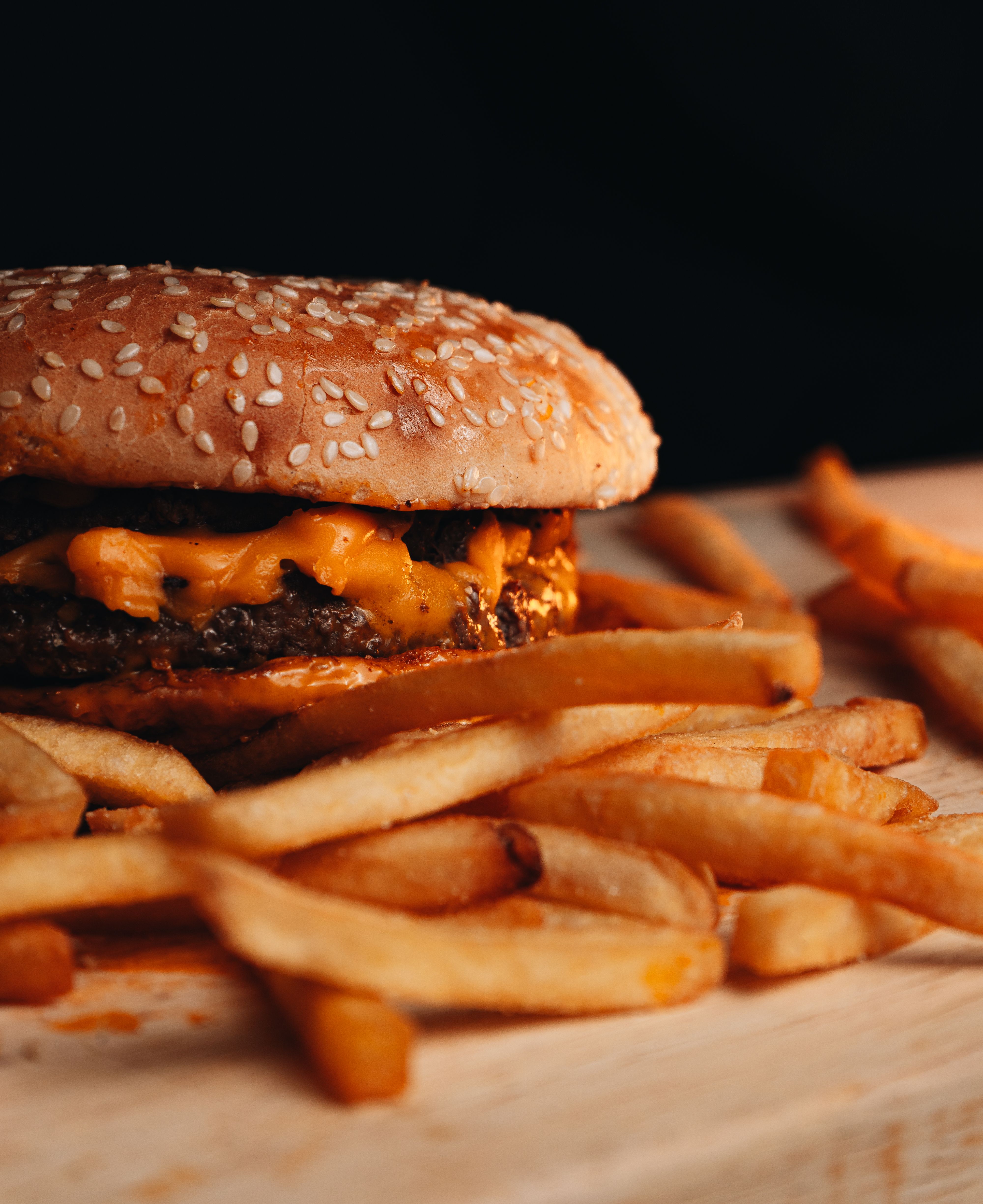 Close-up of a cheeseburger with fries on a wooden board, ideal for food photography.