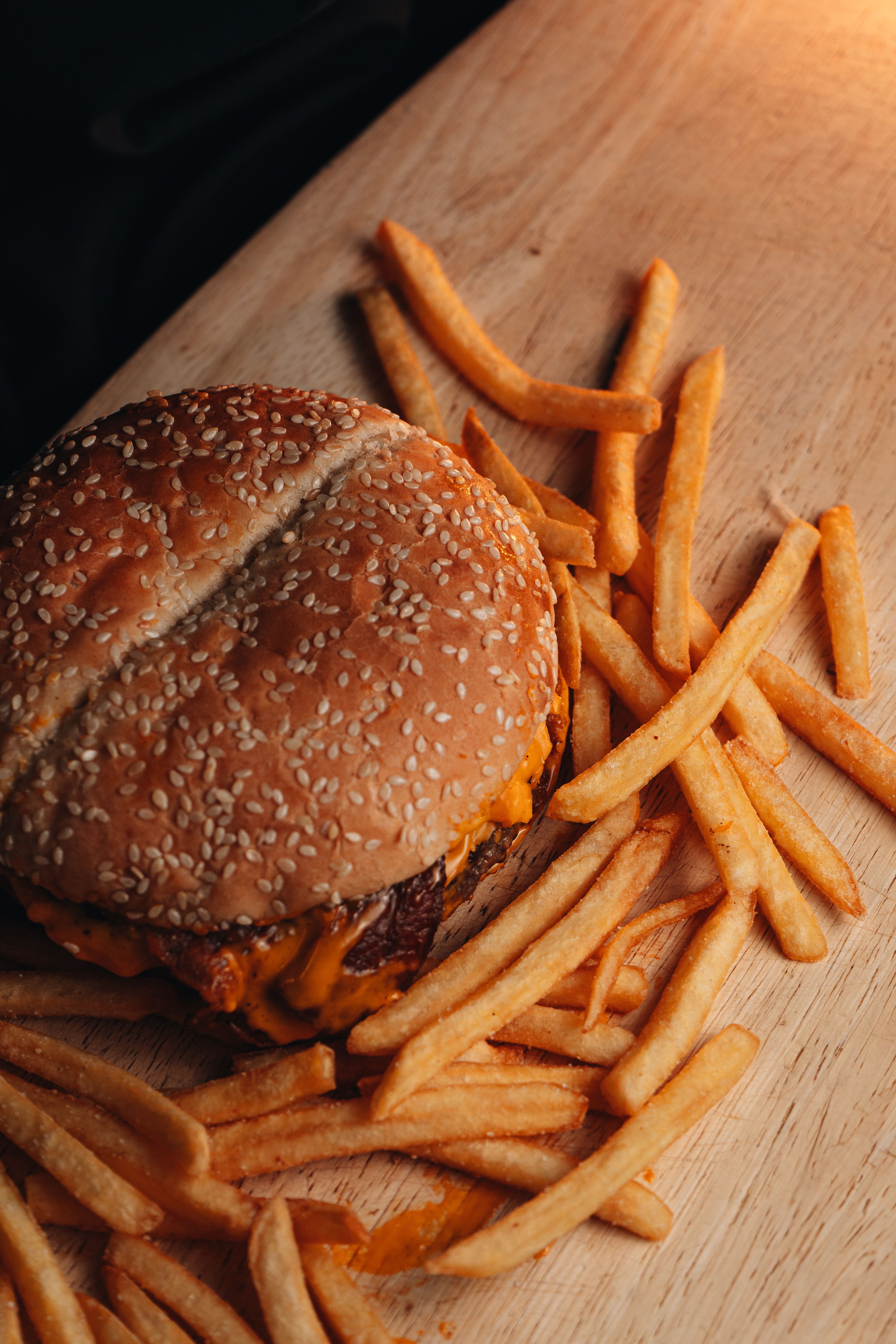 Mouthwatering cheeseburger with crispy fries served on a wooden board, perfect for lunch.