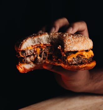 A close-up shot of a cheeseburger with a bite taken, held against a dark background.