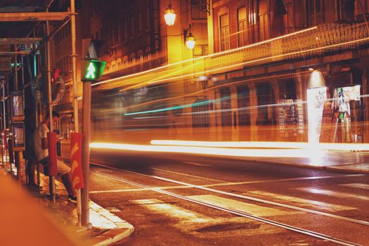 City street at night with motion blur from fast-moving lights, depicting urban life.