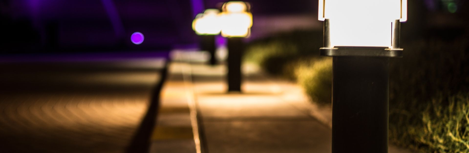 A scenic night view of illuminated lamp posts lining a paved path with a bokeh effect.