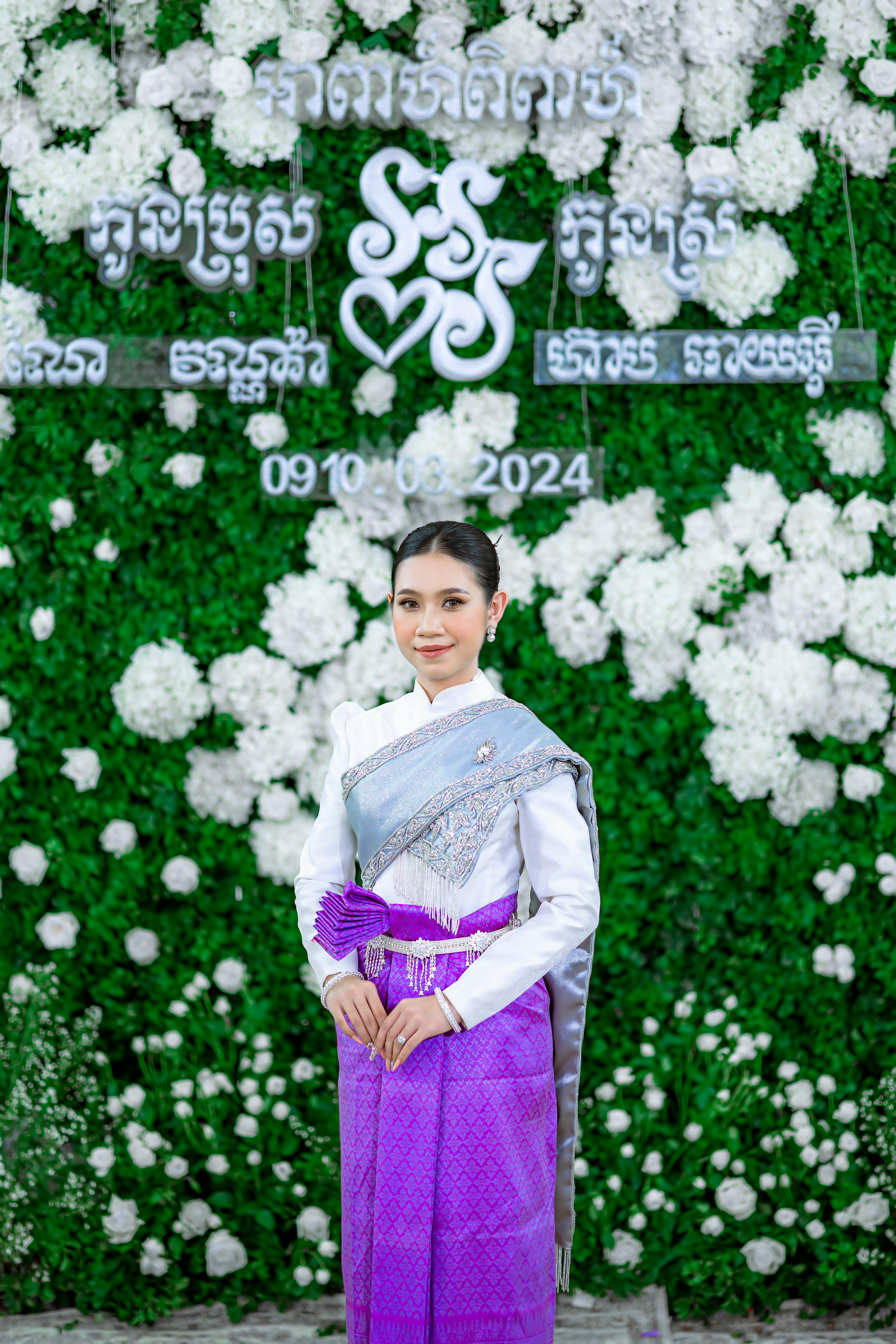 Khmer woman in traditional clothing poses with a floral backdrop, exuding elegance and cultural richness.