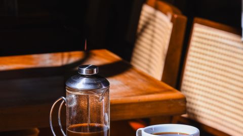 A serene coffee scene with French press and cup on a sunlit table.